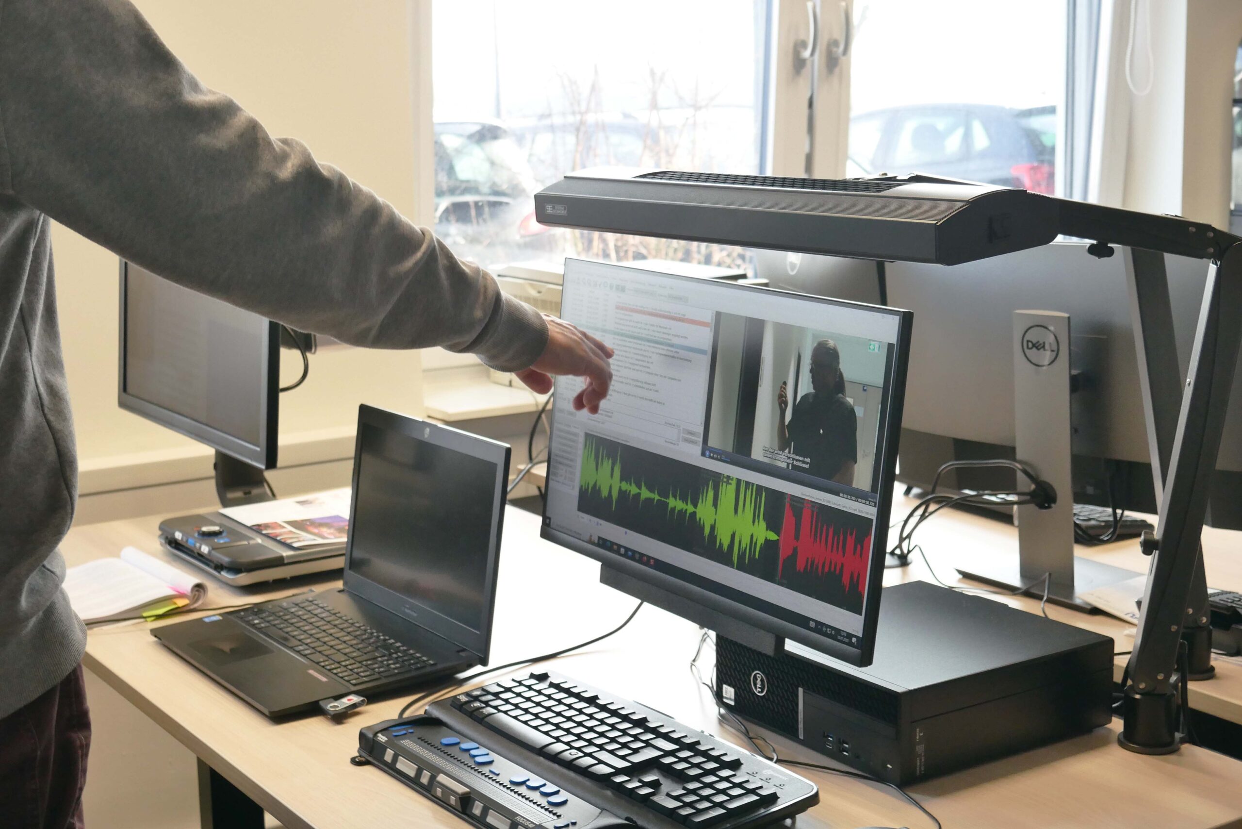 Eine Hand deutet auf den Bildschirm eines Computers auf dem ein Untertitel Programm geöffnet ist.